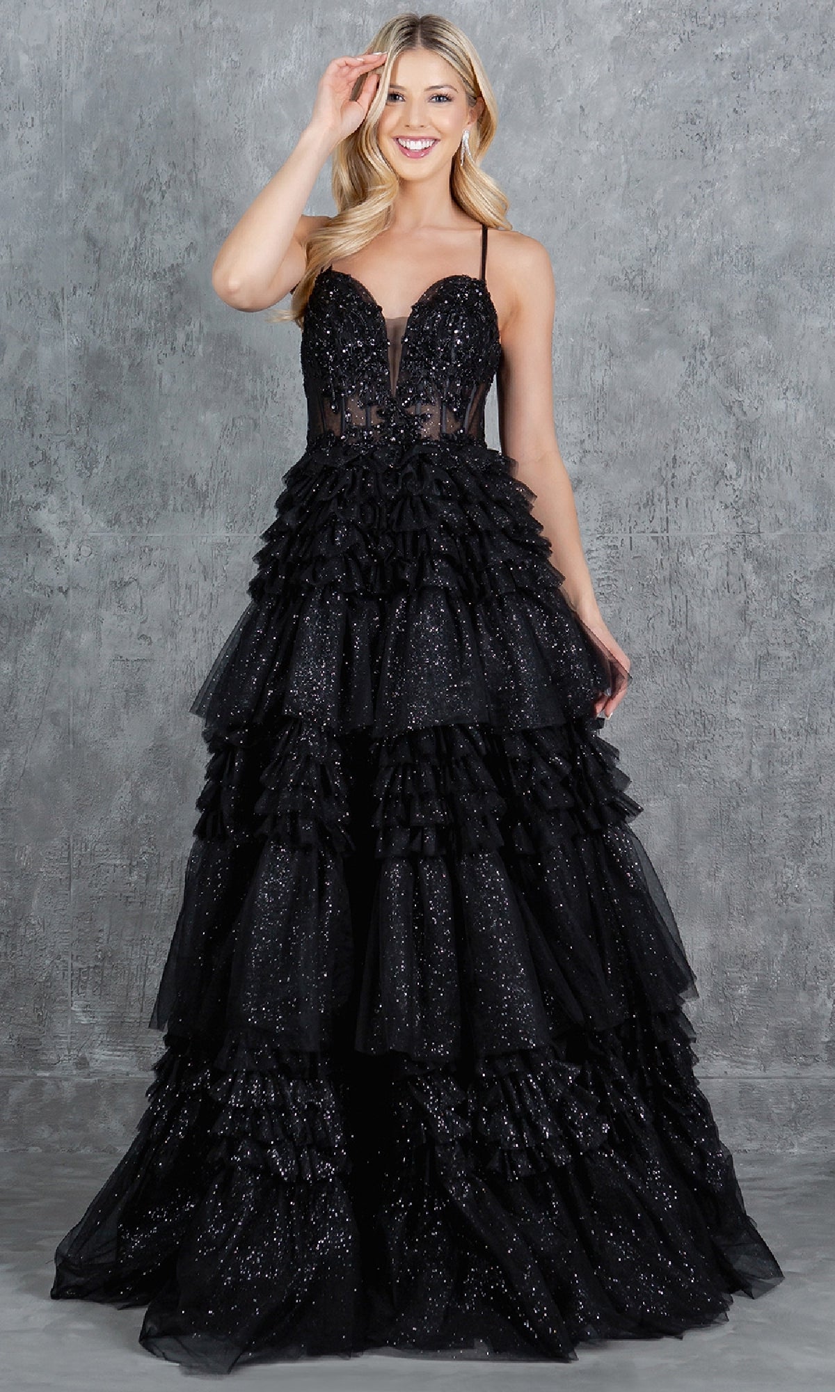 A woman smiles against a textured gray background in the Cinderella Couture 8163J Glitter Prom Ball Gown, a strapless black A-line dress with ruffles, sequins, and a beaded corset bodice—perfect for an unforgettable prom night.